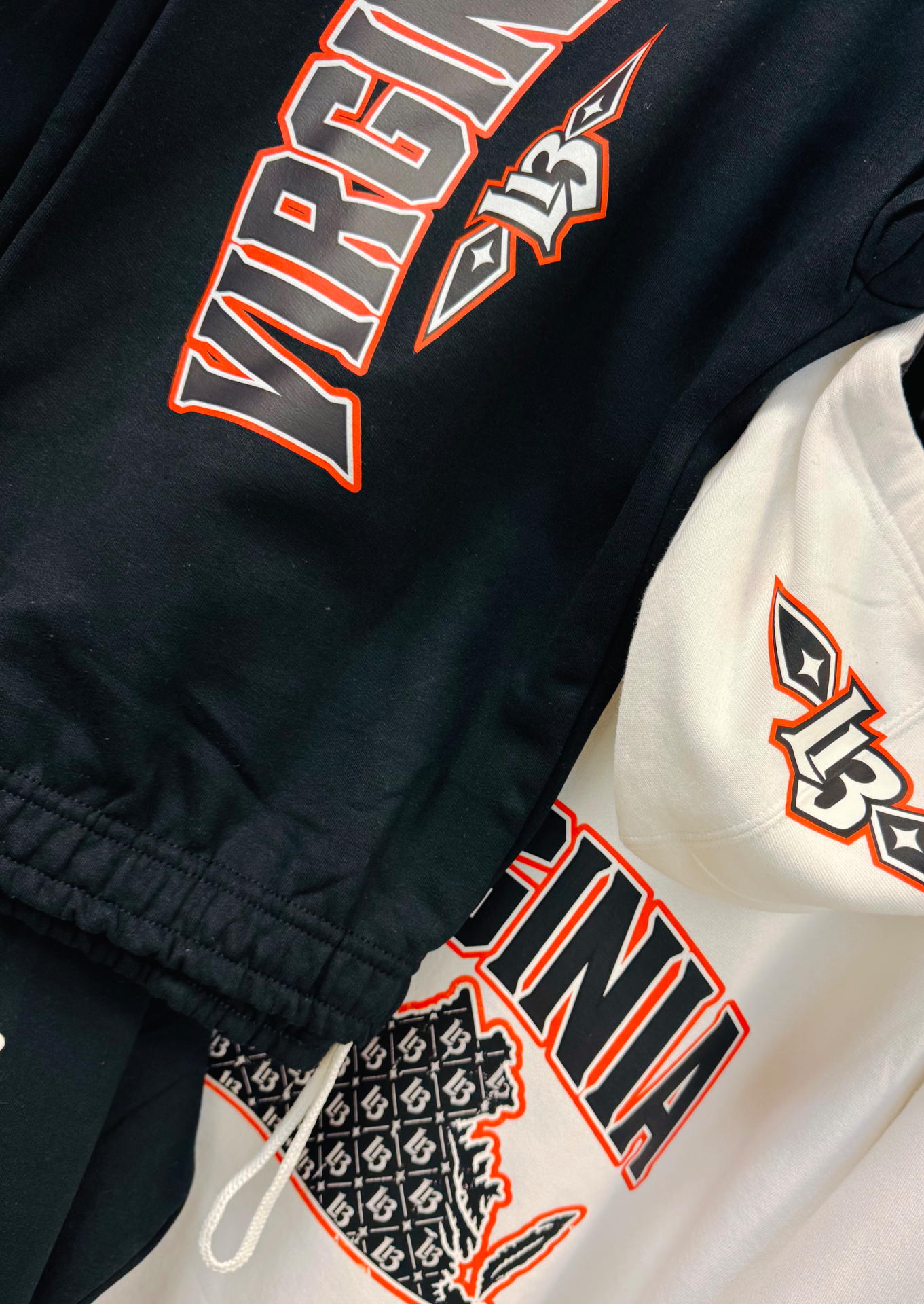 Close photo of the black jogger leg print and white drawcord next to the white hoodie's hood L13 and VIRGINIA print